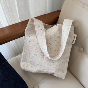 Close-up of a cream canvas tote bag with colorful confetti patterns on a soft leather chair