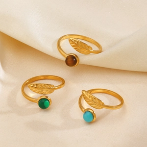 Bagues plumes dorées avec pierres marron, vertes et bleues sur fond en satin soyeux
