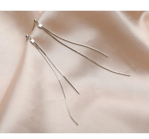Macro view of long silver tassel earrings with snake chains on champagne satin