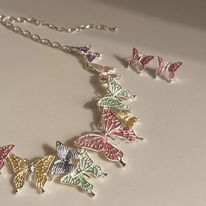 Detail view of colorful enamel butterfly necklace and earring set on white surface