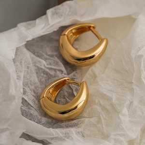 Minimalist gold plated C-shaped earrings on white textured paper with high gloss finish