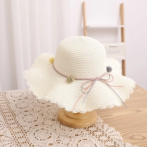 Close-up of kids straw hat featuring wavy lace trim and colorful pom-poms with a bow