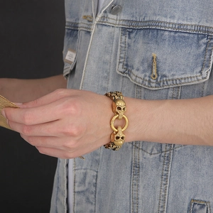 Close-up of gold punk skull bracelet with dual rings on blue denim fabric background