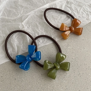 Three elegant acrylic bow hair ties in amber, blue, and green on a minimalist background