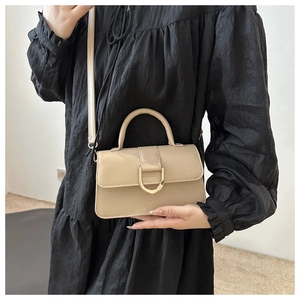 Dettaglio borsa beige in pelle PU con fibbia a D dorata su un elegante abito nero