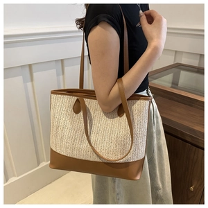 Detail of hand-woven straw tote bag with brown leather trim shown on model