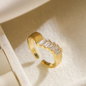 Gold-plated open ring with five rectangular zircon stones on a beige velvet surface