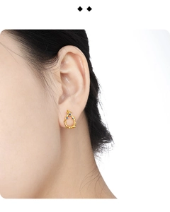 Close-up of irregular gold vine earrings with blue zirconia stones worn by a model