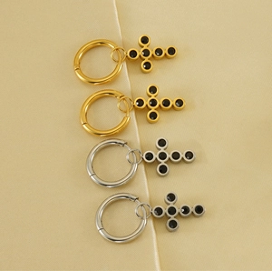Detailed view of gold and silver cross hoop earrings with black zircon stones on silk