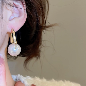 Close-up of elegant gold U-shaped hoop earrings featuring a large round white pearl drop
