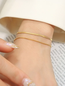 Close-up of a layered gold snake chain and blade chain bracelet on a wrist