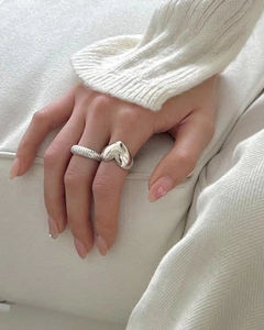 Close-up of minimalist 925 sterling silver puffy heart ring and textured band on finger