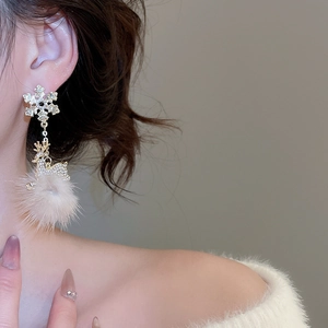 Close-up of Christmas deer earrings with snowflake studs and soft white plush pom poms