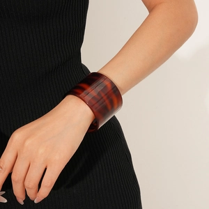 Detailed view of a wide amber tortoiseshell acetate cuff bracelet on a model's wrist