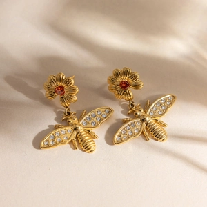 Détail de boucles d'oreilles abeille dorée avec marguerites et zircons rouges éclatants