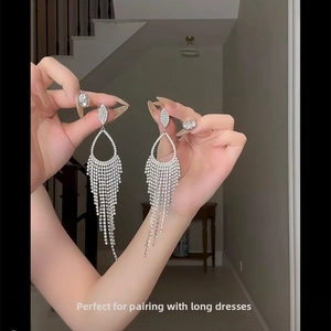 Detailed view of silver-tone tassel earrings with rhinestones held in hand for dinner wear
