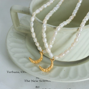 Elegant gold crescent moon pendant with baroque pearls on a vintage book background