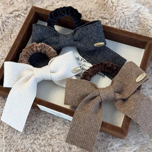 Three elegant knitted bow hair scrunchies in black, cream and brown on a wooden tray