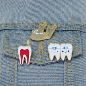 Dental enamel pins featuring jaw and tooth designs pinned on a blue denim pocket