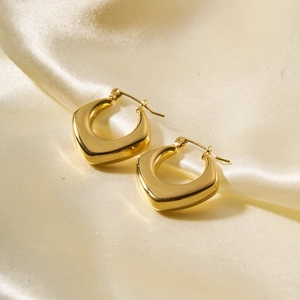 Close-up of gold-plated hollow U-shaped geometric earrings on elegant pearl fabric