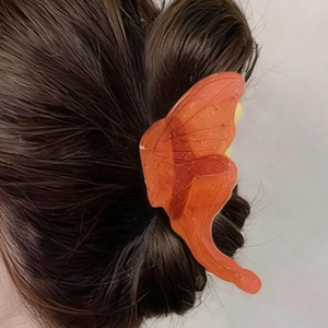 Détail d'une pince à cheveux papillon en résine orange vif avec des textures veinées
