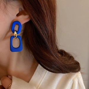 Detail of model wearing geometric Klein blue and gold chain link drop earrings
