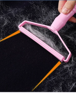 Detail of pink manual lint remover cleaning white pet hair from black fabric texture