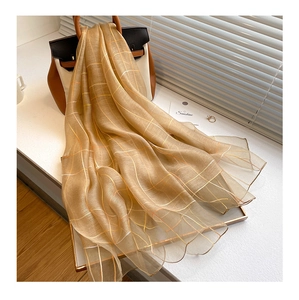 Macro shot of gold striped silk wool thin scarf draped over a wooden tray with a handbag