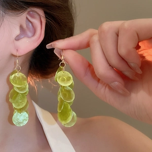 Close-up of long bohemian tassel earrings with lime green shell discs and gold hooks