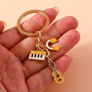 Golden musical keychain with enamel keyboard, guitar and headphone charms on peach background