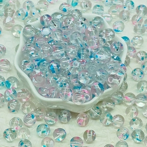 Macro detail of transparent glass beads with blue and pink floral patterns in a small bowl