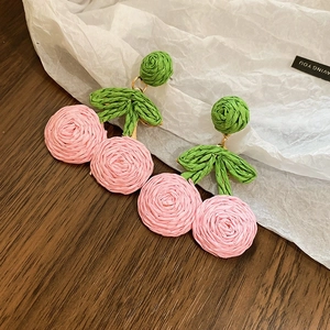 Macro shot of handmade cherry earrings with woven pink fruit and green leaf details