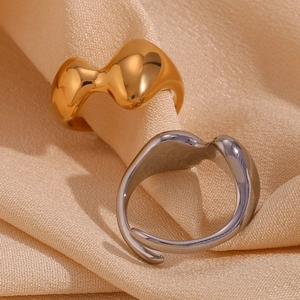 Close-up of irregular wavy rings in gold and silver finish on soft beige fabric