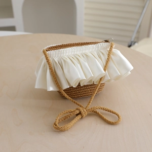 Detail of woven straw handbag with creamy satin ruffles and a brown ribbon bow handle