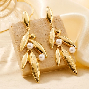 Detail view of gold leaf drop earrings with white pearls on elegant silk and stone background