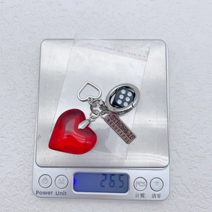 Macro shot of red heart and dice keychain on a digital scale showing weight of 26.5g