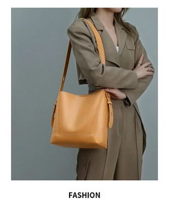 Minimalist mustard yellow leather bucket bag featuring adjustable strap and side tassel detail