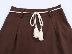 Detail of dark brown trousers featuring a white braided rope belt with tassels