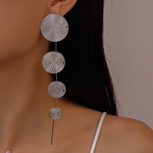Détail de boucles d'oreilles argentées avec disques ronds texturés portées par le modèle
