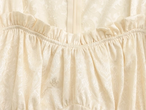 Détail macro du décolleté carré à volants et du tissu jacquard floral sur une robe beige