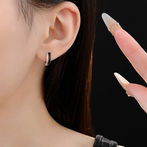 Macro view of black enamel and zircon geometric hoop earrings on a model's ear