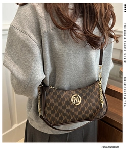 Detail shot of brown monogram shoulder bag with gold chain and metal M logo on grey sweater