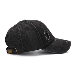 Detail of washed black denim baseball cap showing distressed holes and metal buckle