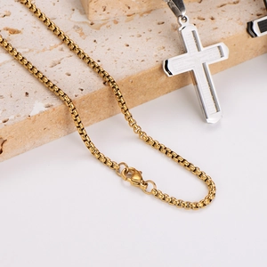 Minimalist gold box chain with silver and gold cross pendant on natural stone base