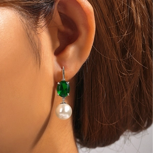 Detail shot of a silver earring featuring an emerald green gemstone and a white pearl drop