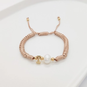 Detail of hand-woven bracelet with white pearl and gold letter T charm on tray