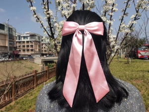 Pink satin bow hair clip styled on long dark hair against a soft outdoor background