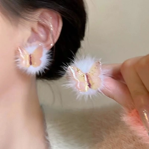 Close-up of fluffy white pompom earrings with pink resin butterflies on model's ear