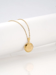 Close-up of gold plated round pendant with letter B and diamond on white stand