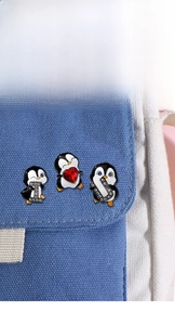 Detailed view of penguin enamel pins set with sparkling rhinestones on blue canvas bag